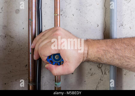 L'homme en utilisant la force pour tourner une vanne d'eau sur un tuyau avec la prenant sa main à l'intérieur dans un local utilitaire dans une vue en gros plan Banque D'Images