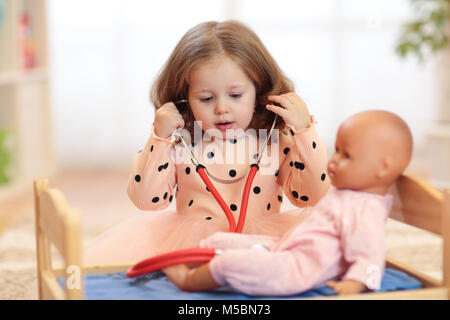 Deux ans girl playing doctor avec poupée dans la pépinière Banque D'Images