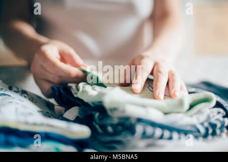 Tri des vêtements de bébé nouveau-né de la mère pour le repassage à domicile dans le cadre des activités quotidiennes dans les services de garde, selective focus Banque D'Images