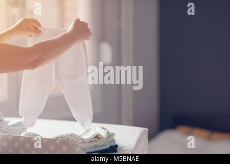 Tri des vêtements de bébé nouveau-né de la mère pour le repassage à domicile dans le cadre des activités quotidiennes dans les services de garde, selective focus Banque D'Images