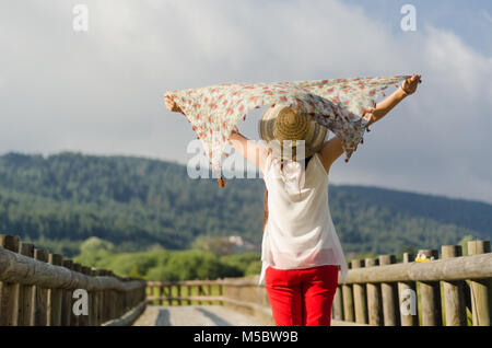 La jeune femme qui tourna son visage dans le vent, leva les mains vers le haut, et ôta son vent dans sa main. Banque D'Images