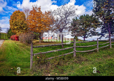 Maison de style Cape en brique rouge avec une clôture en lisse moussue, pelouse verte et feuillage d'automne dans la région de Franconia, NH, USA. Banque D'Images