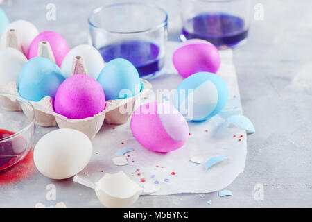 Close-up d'œufs de Pâques peinture en cours. Les tons bleu, rose et violet. Des décorations de Noël sur un fond en béton blanc. Banque D'Images