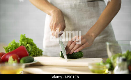 Femme chef concombre en tranches avec un couteau sur planche de bois, les légumes, les séquences Banque D'Images
