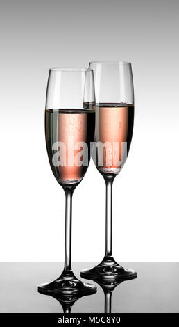 Champagne rose dans deux verres sur une table en verre avec fond dégradé gris-blanc Banque D'Images