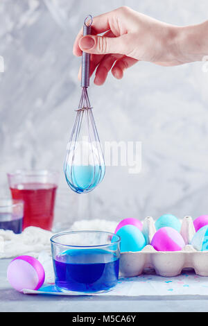 Oeuf de Pâques dans un fouet tenu par la femme. Maison de vacances coloré composition avec colorant alimentaire et du papier bac d'oeufs High key avec copie espace. Banque D'Images