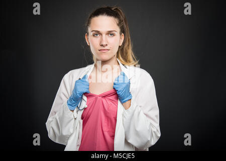 Jeune médecin portrait holding frotte comme geste de super-héros sur fond noir Banque D'Images