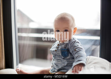 Petit bébé garçon, assis sur un canapé dans un salon ensoleillé, souriant joyeusement Banque D'Images