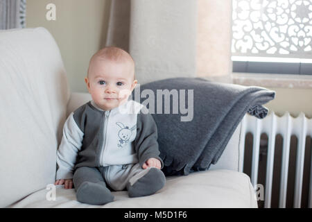 Petit bébé garçon, assis sur un canapé dans un salon ensoleillé, souriant joyeusement Banque D'Images