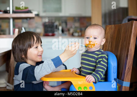 Shirtless Boy Feeding Son Petit Frere Avec Une Cuillere Comme Il Est Assis Sur Un Tabouret Photo Stock Alamy