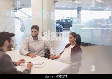 Car salesman talking to pregnant couple dans l'agence de voiture office Banque D'Images