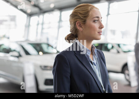 Vendeuse à la voiture voiture rêveuse dans car dealership showroom Banque D'Images