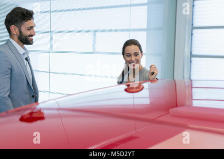 Smiling vendeur de voiture montrant nouvelle voiture rouge à female customer in car dealership showroom Banque D'Images