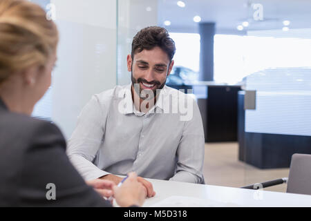 Male customer listening to car saleswoman in car dealership office Banque D'Images