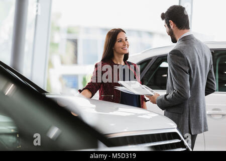 Car saleswoman showing brochure pour male customer in car dealership showroom Banque D'Images