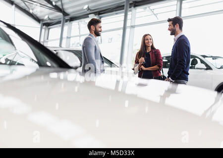 Vendeur de voiture de parler à deux ou trois clients dans car dealership showroom Banque D'Images