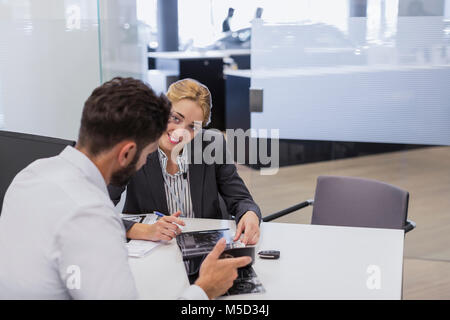 Voiture Smiling saleswoman showing brochure aux clients de sexe masculin dans l'agence de voiture office Banque D'Images