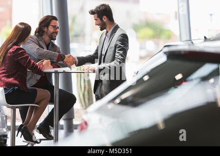 Vendeur de voiture de liaison avec les clients à table en couple car dealership showroom Banque D'Images