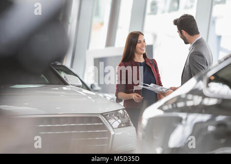 Car saleswoman showing brochure pour male customer in car dealership showroom Banque D'Images