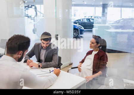 Vendeur de voiture contrat financier expliquant à pregnant couple de clients dans l'agence de voiture office Banque D'Images