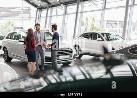 Vendeur de voiture de parler à deux ou trois clients dans car dealership showroom Banque D'Images