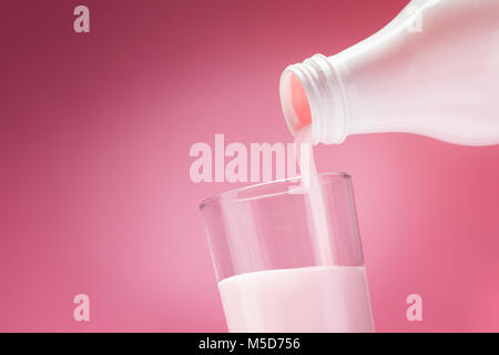 Pouring, à partir d'une bouteille de blanc dans un verre sur un fond rose Banque D'Images