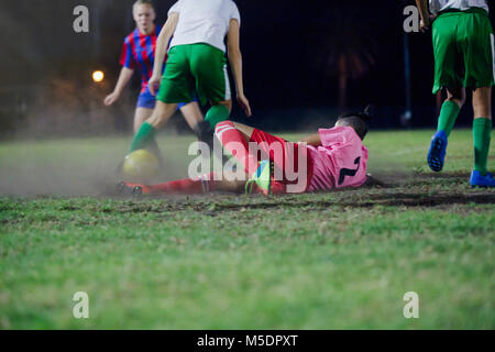 Jeune joueur de soccer féminin chute, coups la balle à jouer au soccer sur terrain de nuit Banque D'Images