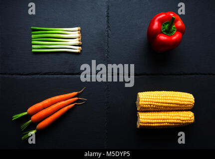 Quatre légumes : oignons, poivrons, carottes, maïs en épi sur la plaque d'ardoise Banque D'Images