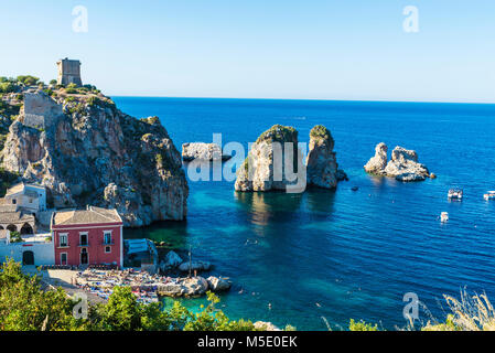 Scopello, Italie - 7 août 2017 : les falaises sur la côte avec la tonnara et les tourelles d'un château médiéval en été avec des gens sur la plage en Scop Banque D'Images