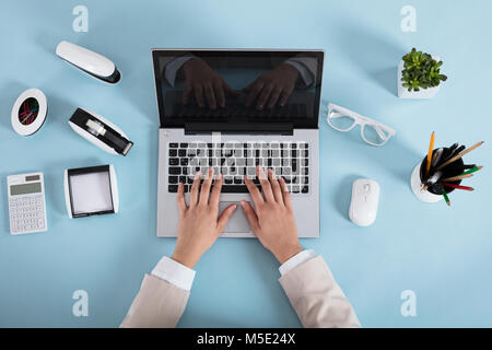 Portrait Of A Woman Typing On Laptop sur le lieu de travail au bureau bleu Banque D'Images