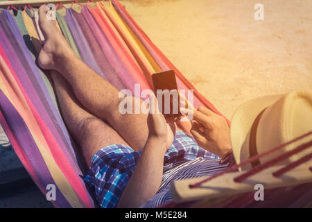 Jeune mec Relaxing In Hammock et à l'aide de téléphone mobile. Les vacances d'été et de la technologie concepts.