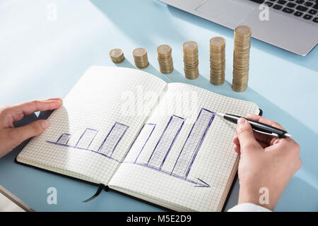 Close-up de l'homme d'affaires graphique Dessin sur Carnet de notes avec des piles de pièces de monnaie sur le bureau Banque D'Images
