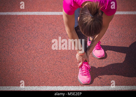 Female jogger mains sur pied. Elle ressent la douleur comme la cheville ou le pied est cassé ou tordu. Accident sur une piste de course au cours de l'exercice matinal. Spo Banque D'Images