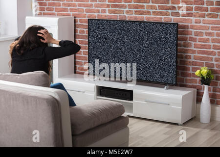Vue arrière d'une femme Obtenir frustré avec Glitch écran de télévision à la maison Banque D'Images