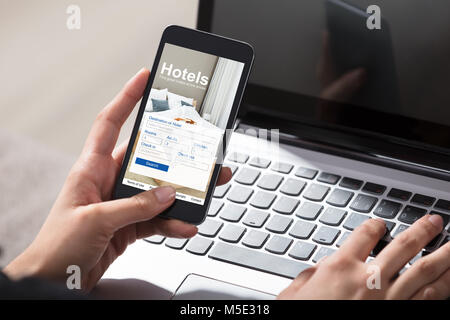 Close-up d'une personne pour réserver des hôtels à l'aide d'un téléphone cellulaire et ordinateur portable Banque D'Images