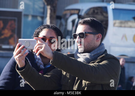 Un jeune couple de prendre un avec un smartphone selfies portant des lunettes de soleil en hiver à Trafalgar Square, Londres, portant des vêtements d'hiver Banque D'Images