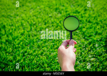 Close up of female hand holding magnifying glass contre fond d'herbe verte. L'espace pour copier. Banque D'Images