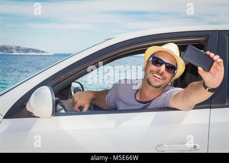 Portrait of young tourist guy en tenant avec selfies smart phone depuis le siège du conducteur. Dans le fond de l'océan. Voyages et transport concepts. Banque D'Images