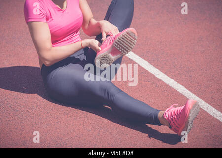 Female jogger mains sur pied. Elle ressent la douleur comme la cheville ou le pied est cassé ou tordu. Accident sur une piste de course au cours de l'exercice matinal. Spo Banque D'Images