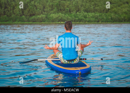 Vue arrière de l'homme faisant du yoga sur le conseil sup avec palettes. Poser lotus méditatif Banque D'Images
