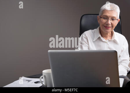 Satisfait senior business woman lu quelques nouvelles sur son laptop in office Banque D'Images
