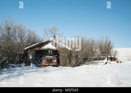 Le Comté de Wheatland (Alberta), Canada. Garage ferme abandonnée avec toit s'est effondré sur un chariot sur la prairie en hiver. Banque D'Images