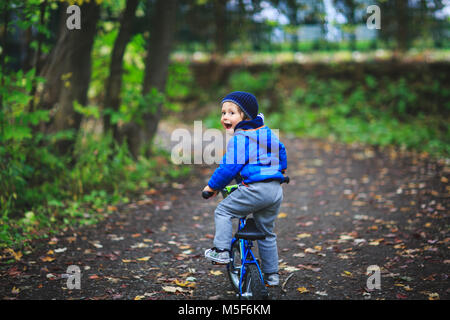 Amazing kid garçon sur un vélo au chemin forestier au printemps ou automne. Cute boy apprendre à circuler à bicyclette sur un chemin forestier. Adorable enfant s'amusant Banque D'Images