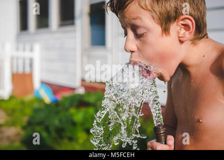 Un garçon de 10 ans boit de l'eau d'un tuyau d'eau sur une journée ensoleillée Banque D'Images