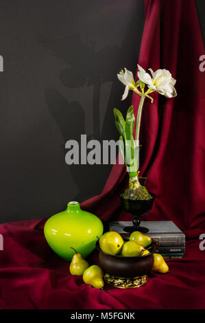 Encore une vie de poires, une fleur, un vase et composée de livres verts et jaunes contraste sur un fond drapé rouge. Banque D'Images