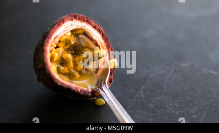 Delicious fresh fruit juteux, maracuja moitié avec spoon gros plan, arrière-plan sombre. La moitié de la passion bien mûrs, granadilla, chair jaune, des graines noires. Banque D'Images