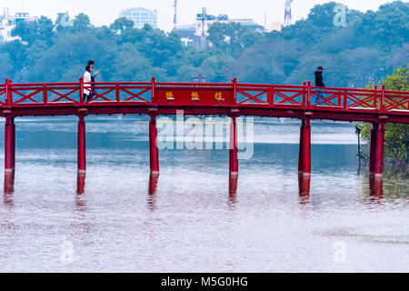 Un jeune couple marche arcoss l'emblématique pont Huc peint rouge sur Ho Hoan Kiem, Hanoi, Vietnam, qui mène à la Tanière Confucius Temple Ngoc Son. Banque D'Images