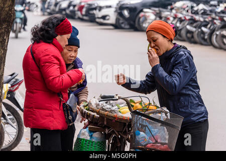 Un vendeur de fruits vietnamiens propose un échantillon d'un client d'orange pour elle d'essayer à Hanoi, Vietnam. Banque D'Images