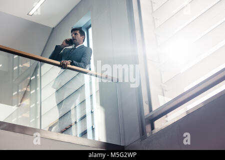 Young parle du corridor sur son téléphone cellulaire. Male executive incliné sur une barre d'immeuble de bureaux et de faire appel. Banque D'Images