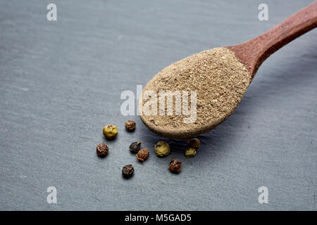 Vue de dessus d'une cuillère en bois plein de grind poudre de poivre noir entouré de noir, blanc, jaune et rouge piment isolé sur fond gris, shallo Banque D'Images